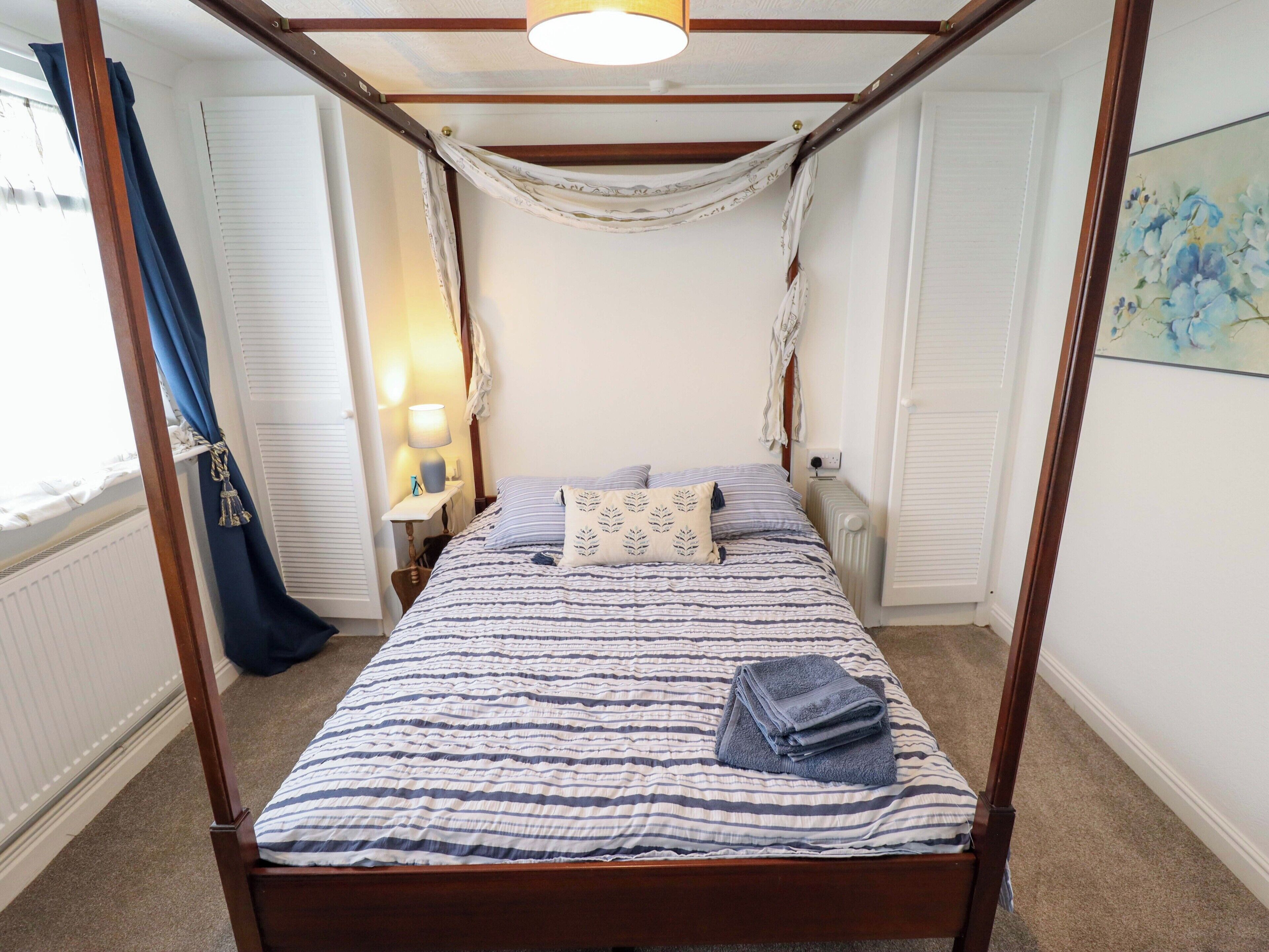 A four-poster bed with a striped bedspread, a bedside table with a lamp, and a radiator.