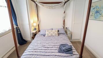 A four-poster bed with a striped bedspread, a bedside table with a lamp, and a radiator.