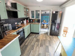 A modern kitchen with a wood floor, green cabinets, and a dining area with a table and chairs. - Four Seasons (Grimsby)