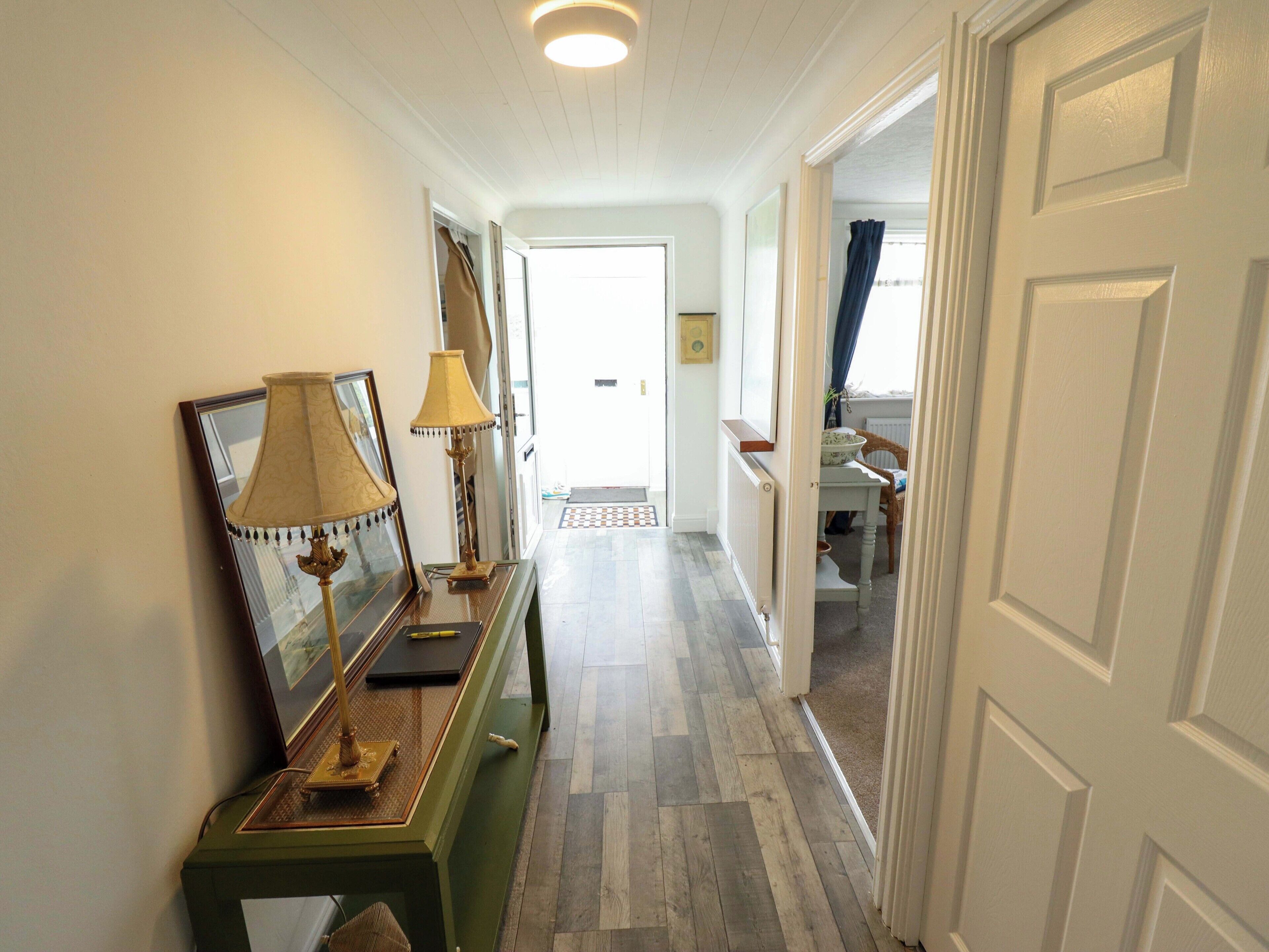 A hallway with a green console table, two lamps, and a door leading to another room.