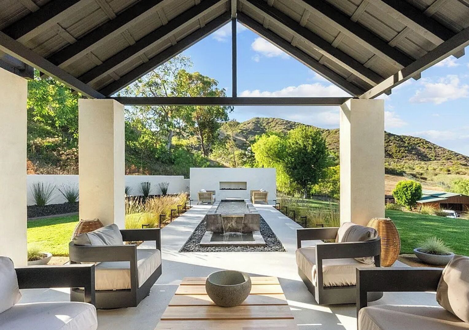 A covered outdoor seating area with a fire pit, sofas, and a view of a landscaped garden.. Malibu Ranch Villa with separate Guest House