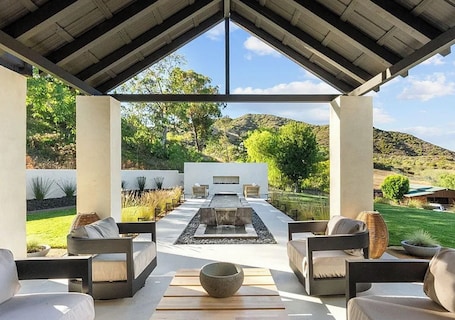 A covered outdoor seating area with a fire pit, sofas, and a view of a landscaped garden.. Malibu Ranch Villa with separate Guest House