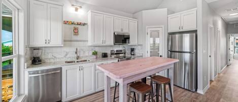 Cocina moderna con armarios blancos, electrodomésticos de acero inoxidable, una barra de madera y vistas al exterior.