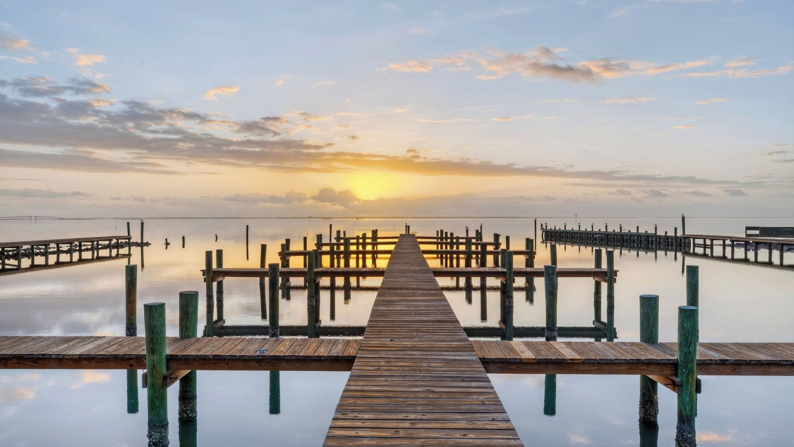 A wooden pier extending into calm water with a sunset in the background.