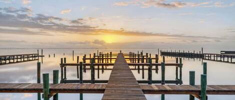A wooden pier extending into calm water with a sunset in the background.