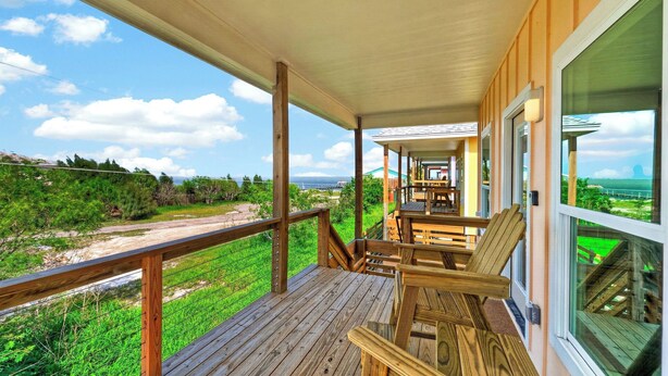 Una terraza de madera con mobiliario exterior, un espacio cubierto y vista a la playa y al océano.