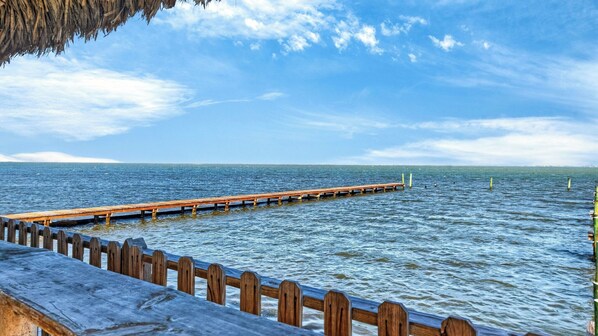 A wooden pier extending into calm water, a clear sky, and a distant shoreline. - Black Drum by Avantstay Water Views Wraparound Decks Pool Access Laguna Madre + Padre Island (Corpus Christi)