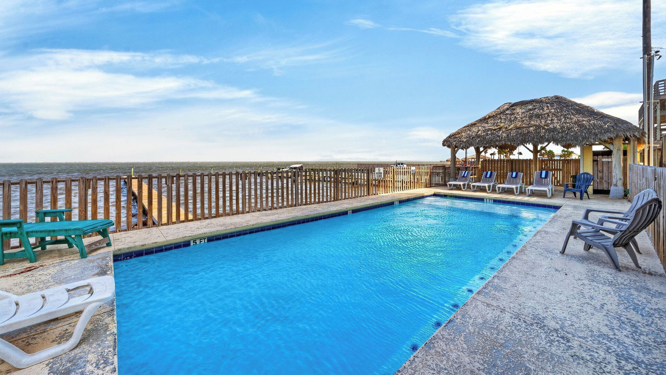 Une piscine avec des chaises longues, une terrasse en bois et une vue sur l’océan.