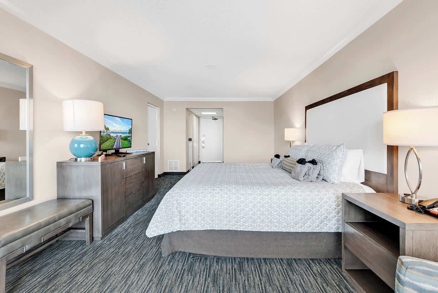 A hotel room with a large bed, a desk with a computer, a TV, and a mirror.