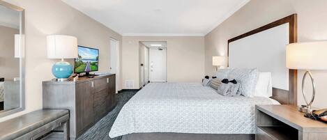 A hotel room with a large bed, a desk with a computer, a TV, and a mirror.