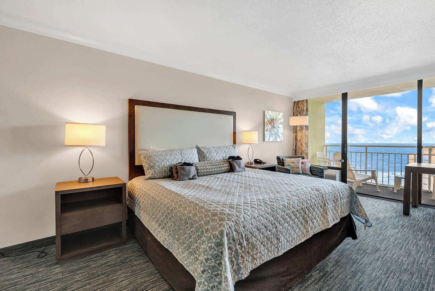 Een hotelkamer met een groot bed, nachtkastjes, uitzicht op zee en een balkon.