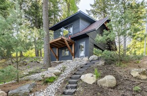 Une maison moderne dotée d’une terrasse en bois, d’un escalier en pierre et surplombant une forêt.