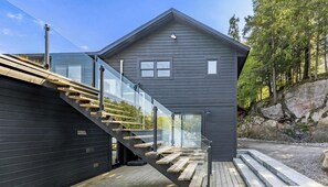 A modern house with a glass staircase, a wooden deck, and a view of a forested area.