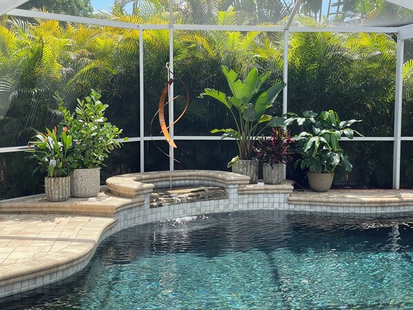 A pool with a tiled edge, surrounded by potted plants, and a white canopy overhead.
