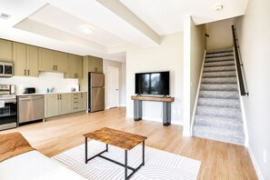 Une cuisine moderne équipée d’appareils électroménagers en acier inoxydable, un coin repas avec une table en bois et un escalier menant à l’étage supérieur.