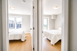 Une chambre avec deux lits, une grande fenêtre et une porte donnant sur une autre pièce.