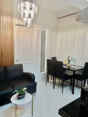 Ein modernes Wohnzimmer mit einem schwarzen Sofa, einem Esstisch mit Stühlen, einer Chandelier und einem Topf mit Pflanze.