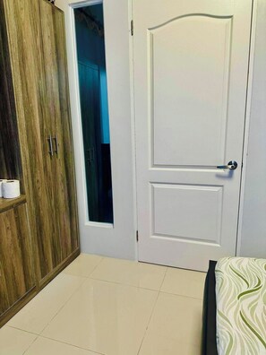 A bedroom with a wooden wardrobe, a white door, and a bed with a patterned bedspread. -     “Modern 1BR Condo – Steps from Beaches & Airport” (Lapu-Lapu)