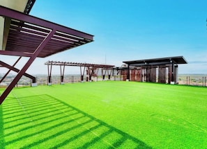 Eine Dachterrasse mit Kunstgrasanlage, Pergolen und Gebäudestruktur.