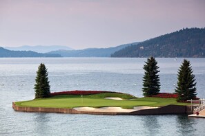 A golf course with a water hazard, two tall trees, and a distant mountain range. - Chateau CDA | Quick Drive to Restaurants & Coeur d'Alene Lake! (Coeur d'Alene)