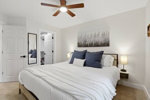 A bedroom with a bed, a ceiling fan, a nightstand with a lamp, a door, and a wall-mounted artwork. - Chateau CDA | Quick Drive to Restaurants & Coeur d'Alene Lake! (Coeur d'Alene)