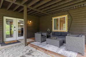 A covered outdoor seating area with wicker furniture, a sliding glass door, and a window with a wooden frame. - Chateau CDA | Quick Drive to Restaurants & Coeur d'Alene Lake! (Coeur d'Alene)