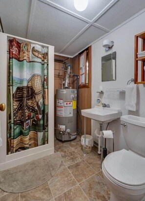 A bathroom with a toilet, sink, shower, and a water heater. - Birch at Hiawatha Cabins (Munising Township)