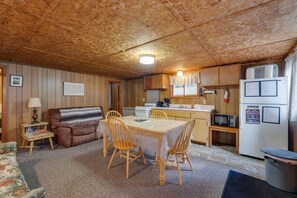Une chambre confortable, aménagée dans le style d’un chalet, avec un plafond en bois, une table à manger avec des chaises, un canapé et un petit coin cuisine équipé d’un réfrigérateur, d’un four à micro-ondes et d’une machine à café.