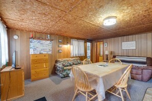 A cozy room with a wooden ceiling, a dining table with chairs, a sofa, a cabinet with drawers, and a lamp. - Birch at Hiawatha Cabins (Munising Township)