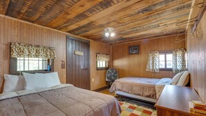 Une pièce aux murs et au plafond en bois, avec deux lits, un bureau et un ventilateur.