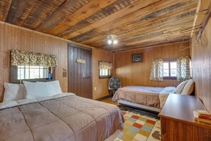 Ein Zimmer mit Holzwänden und -decke, zwei Betten, einem Schreibtisch und einem Ventilator.
