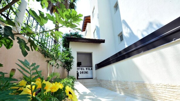 Kapea polku johtaa rakennukseen, jonka yläpuolella on kyltti, jossa lukee: ”OTEL VILA DRINI”.
