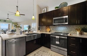 Une cuisine moderne avec des meubles de couleur sombre, des appareils électroménagers en acier inoxydable et des luminaires suspendus.