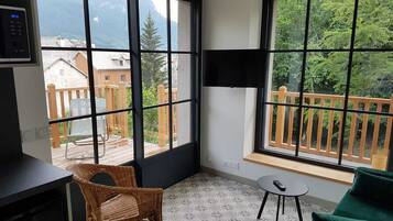 A room with large windows, a wicker chair, a small table, and a green sofa.