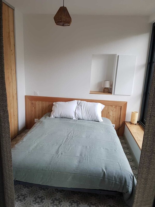 A bedroom with a bed, a hanging light fixture, a mirror, and a window. - Stunning view from the Briançon T1 (Briançon)