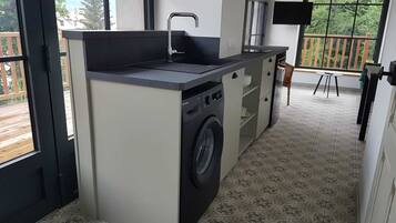 A compact kitchen with a washing machine, a sink, and a small dining area with a view.