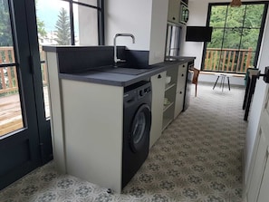 Eine kompakte Küche mit Waschmaschine, Spüle und einer kleinen Essecke mit Blick.