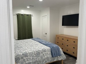 Ein Schlafzimmer mit einem Bett, einer Kommode, einer Tür und einem Fernseher an der Wand.