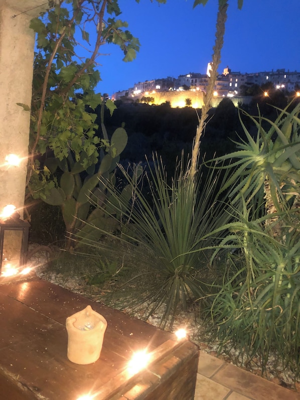 Eine Terrasse mit Tisch, Pflanzen und Blick auf Gebäude im Dämmerlicht.