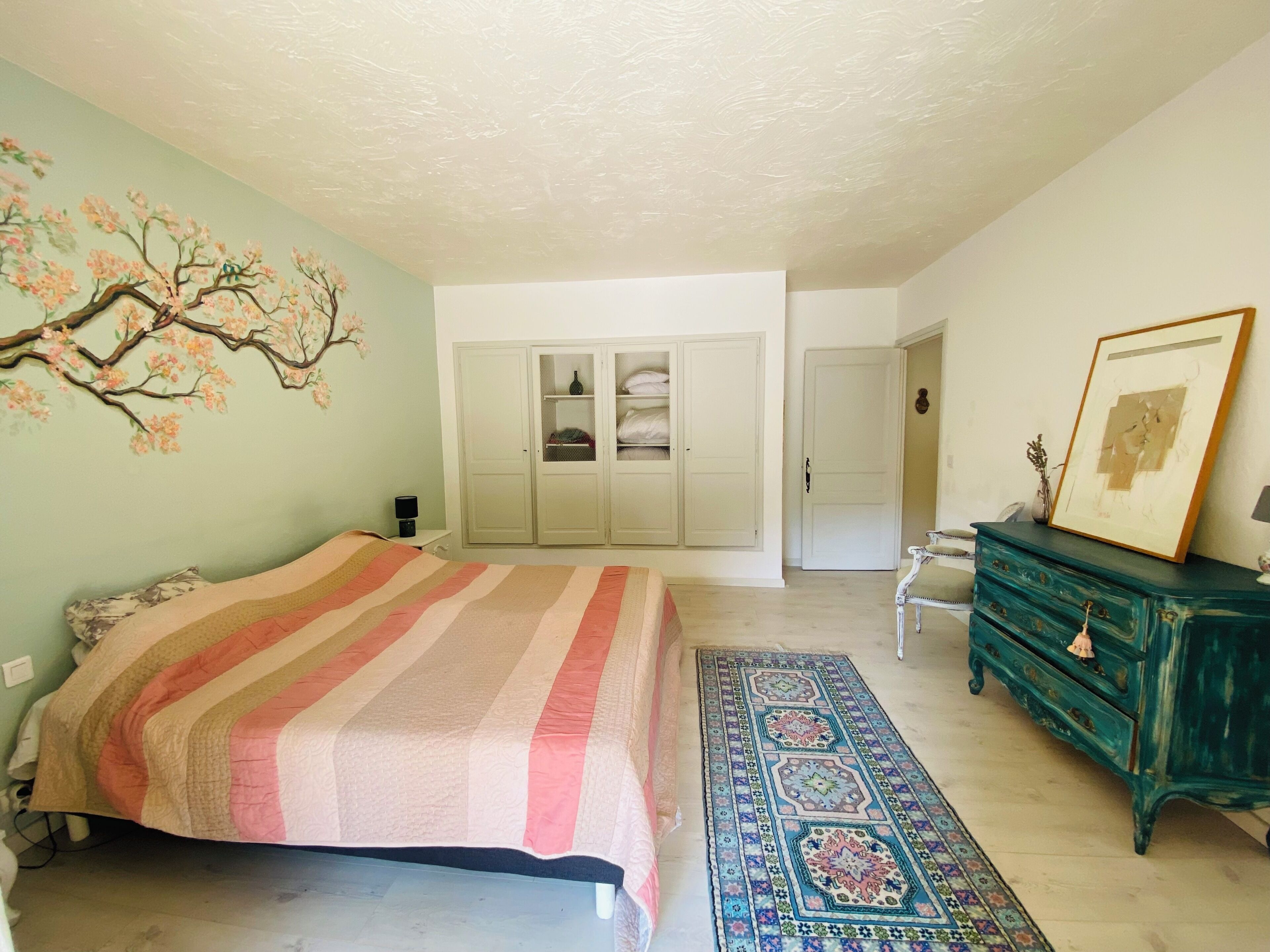 A bedroom with a bed, wardrobe, dresser, and a patterned rug.