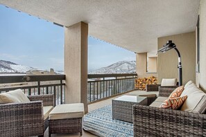 Ein Balkon mit Korbmöbeln, einem Feuerkorb und Blick auf schneebedeckte Berge.