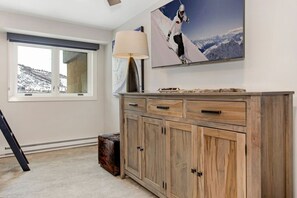 Ein Zimmer mit einem großen Fenster, einem Holfachschrank, einer Lampe und einem Bild in einem Rahmen, das einen Skifahrer zeigt.