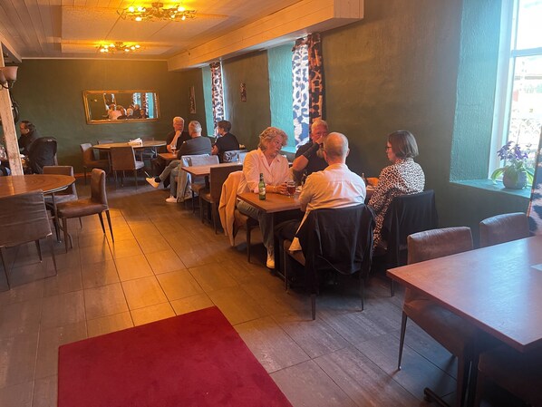 En restaurang med träbord och stolar, en röd matta och en grön vägg med en spegel.