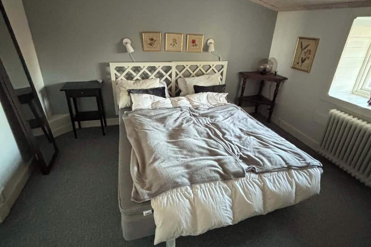 A bedroom with a bed, a nightstand, a chair, a radiator, and a window.