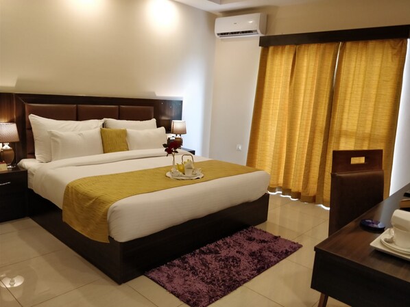 A hotel room with a large bed, a bedside table with a lamp, a coffee table, and a desk with a chair. - D'polo Club & Spa Resort (Dharamshala)