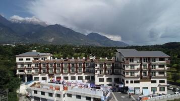 A multi-story hotel with balconies, a parking area, and a mountainous backdrop.