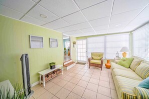 Uma sala de estar com um sofá, uma poltrona, uma mesa pequena e um ar condicionado fixado na parede.