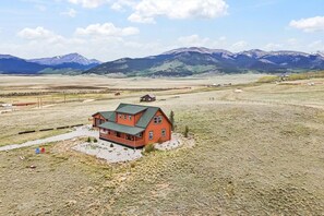 A two-story house with a green roof, surrounded by a vast open field and mountains in the background. - Elk Ridge Retreat | Hot Tub & 360° Views (Park County)