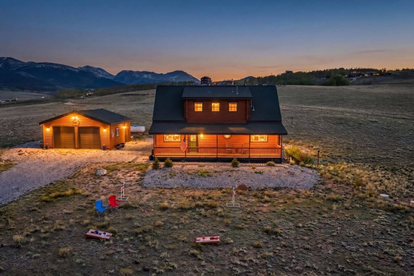 Ein zweistöckiges Blockhaus mit Veranda und Garage, umgeben von einem Schotterweg und einer kleinen Rasenfläche.