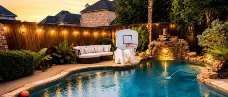 A backyard with a swimming pool, a basketball hoop, and a hot tub.